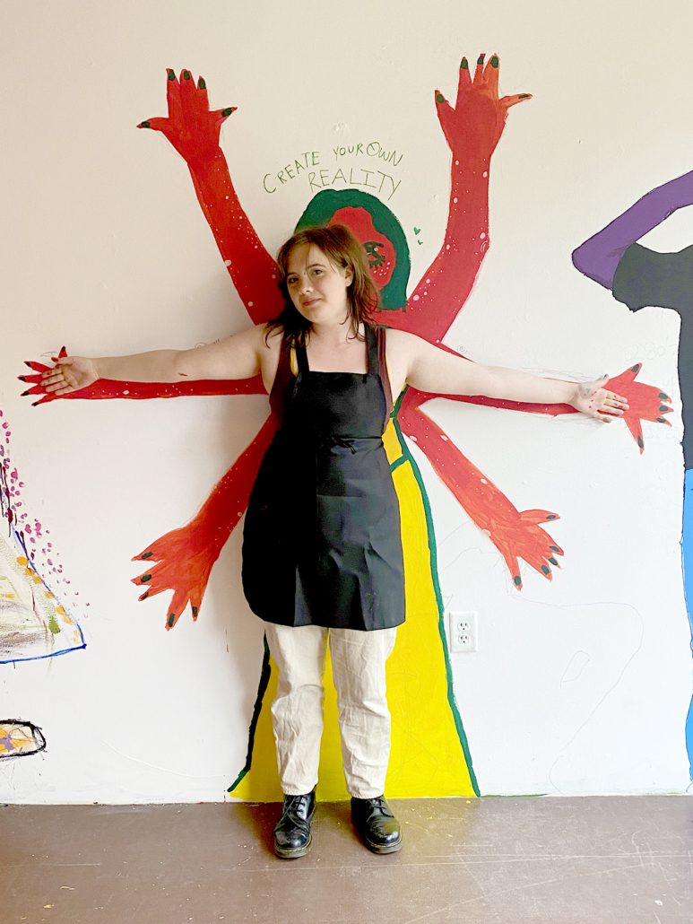 Willow, 17, standing in front of their mural at MCA, arms outstretched